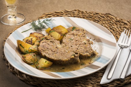 Faschierter Braten - Auf einem runden gestreiften Teller sind 2 Stück des faschierten Braten angerichtet. Neben den Bratenstücke sind als Beilage Erdäpfelelecken angerichtet. Das ganze Gericht ist mit Naturbratensaft übergossen. Rechts neben dem Teller liegen Messer und Gabel auf einer weißen Serviette bereit. (Foto: VrK/Alexander Stiegler - Nicht zur freien Verwendung)