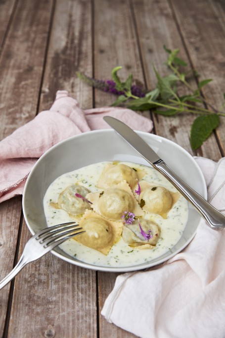 Girschravioli - Auf einem Holztisch steht eine graue Schüssel in der sich eine weiße Kräutersoße befindet. In der Soße sind 6 der Girschravioli angerichtet. (Foto: Barbara Majcan - Nicht zur freien Verwendung)