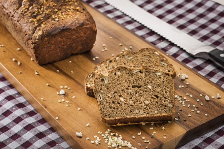 Hanfbrot mit gerösteten Ölsaaten - Auf einem Holzbrett liegen 2 Scheiben des Hanfbrotes leicht überlappend. Die gerösteten Saaten sind im Brot zu erkennen. Im Hintergrund am Holzbrett liegt der Rest des Brotes. (Foto: VrK/Alexander Stiegler - Nicht zur freien Verwendung)