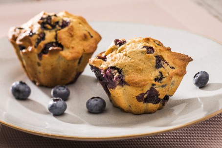 Heidelbeer-Kamut-Muffins - Auf einem weißen Teller sind 2 Muffins angerichtet. Die Heidelbeeren sind als lilafarbige Punkte im Muffin zu erkennen. Auf dem Teller liegen zur Deko einzelne Heidelbeeren verteilt. (Foto: VrK/Alexander Stiegler - Nicht zur freien Verwendung)