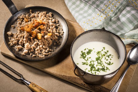 Heidensterz mit saurer Suppe - Der gräuliche Sterz ist in einer kleinen schwarzen Pfanne angerichtet und mit braun angebratenen Grammeln bestreut. Die saure Suppe ist neben der Pfanne in einem kleinen schwarzen Kochtopf angerichtet. Sie ist weiß und mit grob gehackter Petersilie bestreut. (Foto: VrK/Alexander Stiegler - Nicht zur freien Verwendung)