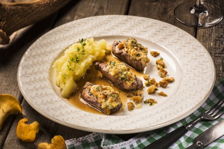 Hirschfilets mit Schwammerlbutter - Auf einem weiß braun gemustertem Teller sind 3 dünne Schnitten des Hirschfilets angerichtet. Auf den Filetstücken ist die Butter mit den Pilzstückchen zu sehen. Neben den drei Stückchen ist eine Portion Stampferdäpfeln platziert. Angebratene Pilze liegen rechts neben den Filetstückchen. (Foto: VrK/Alexander Stiegler - Nicht zur freien Verwendung)