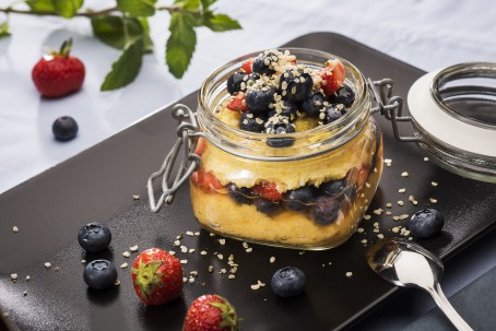 Polenta-Beeren-Frühstück - Auf einem schwarzen Brett steht ein Einmachglas, gefüllt mit gelbfarbenem Polenta, wechselweise geschichtet mit dunklen Heidelbeeren und roten Erdbeeren. Das ganze ist mit gerösteten Ölsaaten garniert. Daneben liegen verschiedene Beeren, ein grüner Zweig und ein Löffel (Foto: VrK/Alexander Stiegler - Nicht zur freien Verwendung)