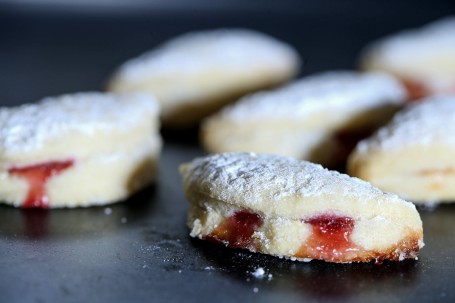 Mostkekse - Auf schwarzem Hintergrund leigen einige mit Staubzucker bestreute zu Halbkreisen zusammengeklappte Mostkekse. Das rote Marmelade quillt etwas hervor. (Foto: Volker Weihbold - Nicht zur freien Verwendung)