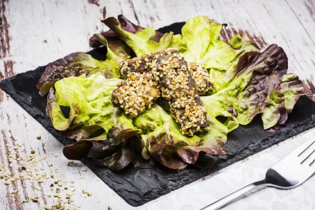 Räuchertofu in Hanfmehl gebacken - Auf einem dunklen Steinteller liegt ein großes grün/lila farbenes Salatblat; daruf liegen drei Stück gebratener Tofu, umhüllt mit einer Panade aus dunklem Hanfmehl und hellen Hanfsamen; daneben liegt eine Gabel und weitere einzelne Hanfsamen (Foto: VrK/Alexander Stiegler - Nicht zur freien Verwendung)