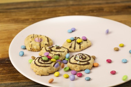 Schnelle Cookies - Auf einem leicht rosa Teller sind 4 Cookies zu sehen. Sie sind mit Schokolade, Smarties und Zuckerperlen verziehrt. Auf dem Teller sind auch noch einige Smarties um die Cookies verstreut. (Foto: Tobias Schneider-Lenz - Nicht zur freien Verwendung)