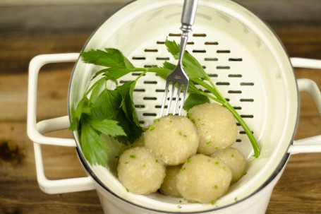 G‘riebene Knödel - In einem weißen Email-Sieb sind ca. 7 kleine Knödel zum Abtropfen bereitgestellt. In einem Knödel steckt eine Gabel. Ein Zweig Maggikraut liegt neben den Knödeln. Die Knödel sind alle leicht mit Schnittlauch bestreut. (Foto: Tobias Schneider-Lenz - Nicht zur freien Verwendung)