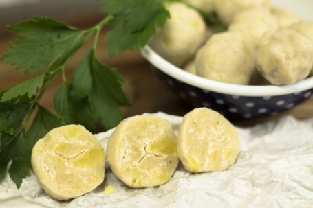 Stauberte Knödel - Auf einem weißen Oberfläche liegen 3 halbe Knödel. Man kann die grobe Struktur gut erkennen. Im Hintergrund steht eine dunkelblaue mit Blümchen gemusterte Email-Schüssel mit vielen Knödeln darin. Ebenso in Hintergrund liegt ein Kräuterzweig. (Foto: Tobias Schneider-Lenz - Nicht zur freien Verwendung)