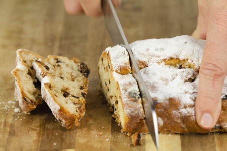 Feiner Topfenstollen - Der hellgelbe Stollen wird am Bild in 2 Zentimeter dicke Scheiben geschnitten. 2 Scheiben sind bereits geschnitten, die Früchte sind darin gut zu erkennen. Der Stollen ist mit Staubzucker bestreut. (Foto: Tobias Schneider-Lenz - Nicht zur freien Verwendung)