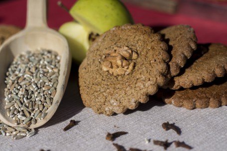 Saftiger Roggenlebkuchen - Vier Stück des Lebkuchens sind schräg aufeinander gestapelt. Jeder der Lebkuchen hat eine halbe Nuss in der Mitte. Der Lebkuchen ist in einer runden Form mit Wellen am Rand ausgestochen. Links neben den Lebkuchen liegt eine Holzmehlschaufel, in der sich Roggenkörner befinden. Im Vordergrund liegen noch einige Nelkenkörner. (Foto: Tobias Schneider-Lenz - Nicht zur freien Verwendung)