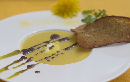 Polentaschaumsupperl mit Frischkäse und Brotchips - In einem großen weißen Suppenteller ist die gelbliche Suppe angerichtet. In der Suppe ist ein Stück Frischkäse zu sehen. Über die Suppe sind einige Streifen Kürbiskernöl gezpgen. Am Rand des Tellers liegen zwei Scheiben der mit Knoblauch und Öl bestrichenen Brotchips. (Foto: Romana Schneider-Lenz - Nicht zur freien Verwendung)