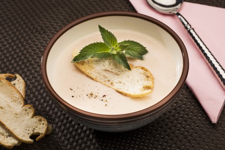 Steirische Schilcherrahmsuppe - In einer weißen Schüssel mit brauem Rand befindet sich die weiße Suppe, garniert mit einer Scheibe Weißbrot und Minze bzw. etwas Pfeffer. Daneben liegen zwei Scheiben Brot und ein Löffel auf einer rosa Serviette. Das ganze befindet sicha uf einem braunen Untergrund (Foto: VrK/Alexander Stiegler - Nicht zur freien Verwendung)