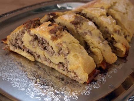 Erdäpfelroulade mit Faschiertem und warmer Schnittlauchsoße - Auf einem silbernen Tablett mit Muster sind einige Stücke der Roulade aufgeschnitten und hintereimander platziert. (Foto: VrK/DI Carina Laschober- Luif - Nicht zur freien Verwendung)