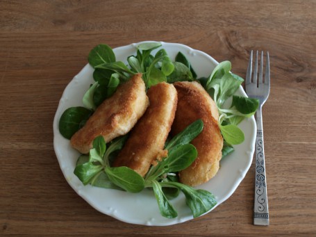 Erdäpfeltascherl „Cordon bleu“ - Auf einer Tischplatte steht ein kleiner weißer Teller. Auf dem Teller ist Feldsalat angerichtet, auf dem Feldsalat liegen drei der panierten Erdäpfeltascherl. Rechts neben dem Teller liegt eine Gabel. (Foto: VrK/DI Carina Laschober- Luif - Nicht zur freien Verwendung)