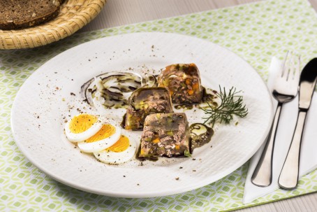 Rindfleischsulz - Auf weißem Teller liegen drei eckige Stücke einer Sulz,daneben liegen drei Eischeiben, garniert mit Zwiebel und Kürbiskernöl und Kräuter. Danebenliegt ein Besteck und ein Brotkorb (Foto: VrK/Alexander Stiegler - Nicht zur freien Verwendung)