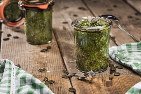 Kürbiskernpesto - Auf einem Holztisch steht ein geöffnetes Glas mit grünfarbenem Pesto, garniert mit Kürbiskernen. Daneben liegt ein weiß/grün kariertes Tuch und ein zweites geschlossenes Glas mit Pesto (Foto: VrK/Alexander Stiegler - Nicht zur freien Verwendung)