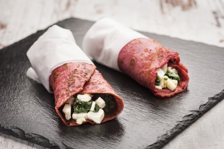 Wrap mit Roten Rüben, Spinat und Käse - Auf einer schwarzen Steinplatte liegen zwei in weißer Serviette gehüllte rotfarbene Wraps, gefüllt mit Schafskäse und grünem Spinat (Foto: VrK/Alexander Stiegler - Nicht zur freien Verwendung)