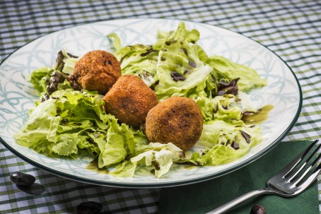 Steirische Käferbohnenbällchen - Auf einem hellen Teller, liegen gebettet auf grünen Blattsalaten, drei braun gebackene Bällchen. Garniert mit Kürbiskernöl (Foto: VrK/Alexander Stiegler - Nicht zur freien Verwendung)
