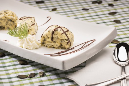 Kürbiskernparfait mit Schokosauce - Auf einem weißen Teller liegen drei Kugeln gelb/grünes Parfait; garniert mit Schokosauce und Schlagobers. Das ganze steht auf einem weiß/grün karierten Tuch auf dem ganze Kürbiskerne liegen. (Foto: VrK/Alexander Stiegler - Nicht zur freien Verwendung)