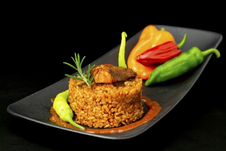 Reisfleisch - Auf einem dunkelgrauen Teller ist das Reisfleisch als Häufchen drapiert, ganiert mit Paprika- und Pfefferonischoten, einer roten Sauce. Garniert mit Kräuter. (Foto: Tobias Schneider-Linz - Nicht zur freien Verwendung)