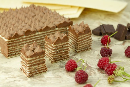 Oblatentorte - Eckige Oblaten und Schokocreme sind abwechselnd aufeinander geschichtet. Auf der obersten Oblate sind Tupfen mit der Schokocreme aufgespritzt. Drei kleine viereckige Stücke sind hergeschnitten und stehen im Vordergrund. Einige Himbeeren liegen als Deko davor. (Foto: Tobias Schneider-Lenz - Nicht zur freien Verfügung)
