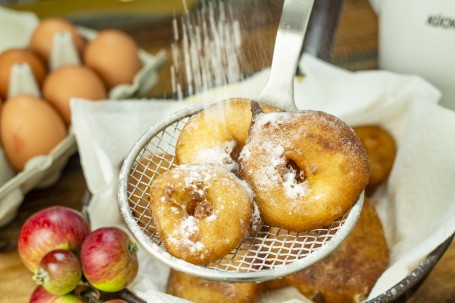 Gebackene Apfelradln - Auf einem Siebschöpfer liegen drei gebacken Apfelradln, die gerade mit Staubzucker bestreut werden. (Foto: Tobias Schneider-Lenz - Nicht zur freien Verfügung)