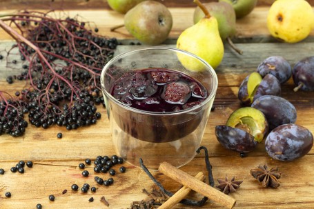 Holler-Zwetschken-Röster - In einem kleinen Glas ist eine Portion des Holler-Zwetschken-Rösters angerichtet. Rundherum liegen Hollunderbeeren, Zwetschken und Gewürze als Deko. (Foto: Tobias Schneider-Lenz - Nicht zur freien Verwendung)