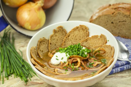 Brotsuppe - In einer weißen Schüssel sind hellbraune Brotscheiben aufgelegt, mit Suppe übergossen, mit Schnittlauch, goldgelb gebratenen Zwiebelringen und Sauerrahm garniert. (Foto: Tobias Schneider-Lenz - Nicht zur freien Verwendung)