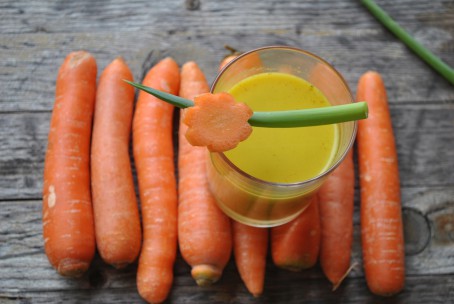 Karottencremesuppe - Auf Karotten, die in einer Reihe aufgelegt sind, steht ein kleines Glas in dem sich die orange-gelbe Karottencremesuppe befindet. Als Garnitur ist ein Schnittlauchhalm und ein Karottenstück in Blumenform schräg über das Glas gelegt. (Foto: Romana Schneider-Lenz - Nicht zur freien Verwendung)