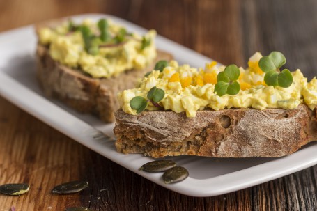 Eier-Kürbiskern-Aufstrich - Auf einem weißen Teller liegen zwei dicke Scheiben Schwarzbrot. Diese Scheiben sind mi´t dem gelblichen Aufstrich dick bestrichen. Als Deko sind einige Kräuter über den Aufstrich gestreut. (Foto: Tobias Schneider-Lenz - Nicht zur freien Verwendung)