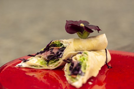 Fladenbrot - 2 gerollte Fladenbrote gefüllt mit Fleisch, Salat und einer weißen Soße liegen schräg übereinander auf einem roten Teller. Auf der oberen Fladenbrotrolle ist eine schöne lilafarbene Blume platziert. (Foto: Tobias Schneider-Lenz - Nicht zur freien Verwendung)