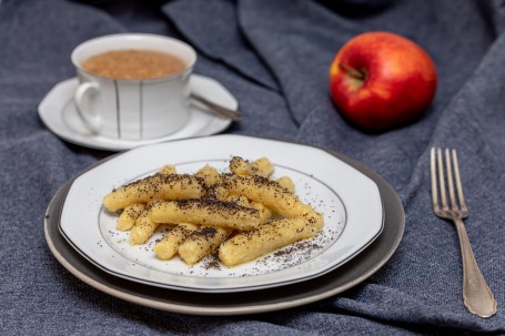 Schupfnudeln mit Mohn - Auf einem weißen Teller liegen gelbfarbene, fingerdicke Nudeln garniert mit geriebenen Mohn, daneben eine Tasse Kaffe und ein Apfel (Foto: VrK/Achim Mandler Photography - Nicht zur freien Verwendung)