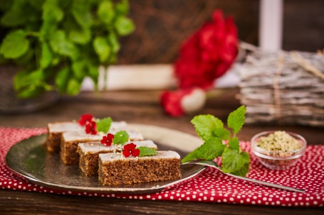 Hanfnüsschen Schnitte - Auf einem roten Tischtuch mit weißen Punkten ist ein silberner Teller. Darauf sind vier Hanfnüsschen Schnitten zu sehen. Diese sind mit roten Blüten und grünen Kräutern verziert. Eine Gabel zum Essen und eine Glasschüssel mit Beilage sind bereitgestellt. (Foto: VrK/Franz Gleiß - Nicht zur freien Verwendung)