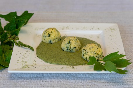 Liebstöcklpolenta - Auf einem weißen eckigen Teller ist eine grüne cremige Soße in der Mitte platziert. In der Soße liegen 3 Polentaknödel. Die Kräuter darin sind gut zu erkennen. Rechts vorne liegt ein Blatt Petersilie als Deko. Auf der linken Seite liegen grüne Kräuter als Deko. (Foto: VrK/Achim Mandler Photography - Nicht zur freien Verwendung)