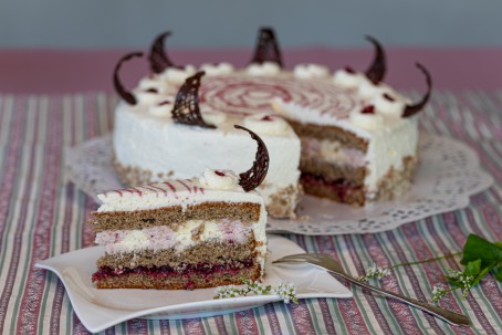 Hadnmehltorte - Auf einem gestreiften Tuch steht ein eckiges, weißes Dessertteller. Auf diesem Teller befindet sich ein Stück der Torte. Sie hat mehrere Schichten und ist mit Schlagobers überzogen und mit einem dekorativen Schokostück verziert. Im Hintergrund steht auf einem runden Tortenteller, das mit einer weißen Spitzenborte abgedeckt ist, der Rest der Torte. (Foto: VrK/Achim Mandler Photography - Nicht zur freien Verwendung)