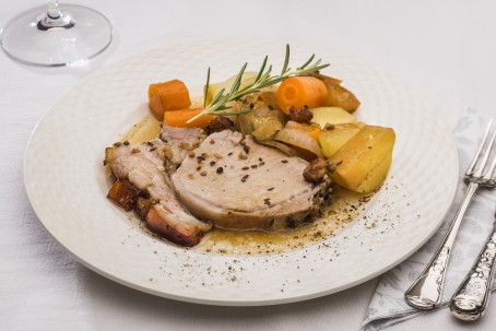 Bauern-Schweinsbraten - Auf einem weißen Hintergrund steht ein weißer runder Teller. Auf dem Teller sind 2 Scheiben magerer Schweinebraten mit knuspriger Kruste angerichtet. Im hinteren Teil des Tellers liegt das gegarte Gemüse und Erdäpfeln. Das Ganze ist mit einem hellbraunen Naturbratensaft übergossen und mit einem Rosmarienzweig garniert. (Foto: VrK/Alexander Stiegler - Nicht zur freien Verwendung)